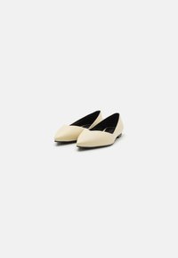 Ballerine a punta in morbida pelle color crema con una texture liscia e design minimalista, dotate di soletta nera e tacco piatto.