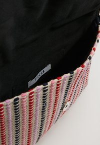 Borsa a strisce colorate realizzata in tessuto intrecciato nei colori rosa, rosso e blu navy, con un interno nero e un'etichetta che riporta la scritta "PIECES." Presenta una chiusura a scatto.