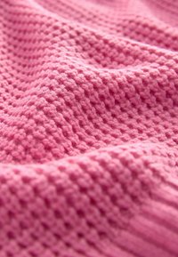 Strickstoff in einem sanften Rosa-Ton, der ein strukturiertes Muster mit erhabenen und flachen Bereichen aufweist, was ein taktiles, gemütliches Erscheinungsbild schafft.