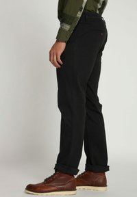 Pantaloni neri con una vestibilità slim e una sottile texture, con risvolti e una tasca sul retro con un bottone decorativo. Stivali marroni stringati.