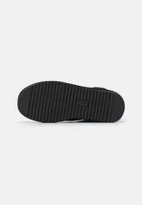 Semelle de chaussure en caoutchouc noir avec des rainures horizontales et une étiquette rectangulaire. Matériau supérieur doux et texturé. Profil légèrement courbé.