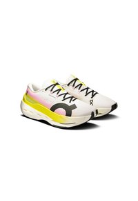 Scarpe sportive con tomaia in rete bianca, accenti rosa sfumati, lettere nere in grassetto, suola intermedia gialla e lacci neri. Suola esterna spessa e bianca.