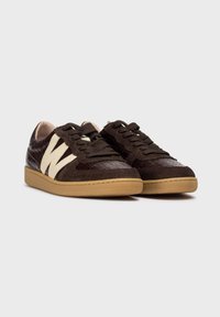 Brązowe sneakersy z teksturowanym, przypominającym skórę zwierząt materiałem oraz gładkimi zamszowymi akcentami. Posiadają kremowe logo i gumową podeszwę.