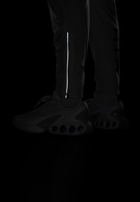 Sorte sportsko med en tekstureret overdel og store luftpuder. Slim-fit sorte bukser med en reflekterende lynlåsdetaile.