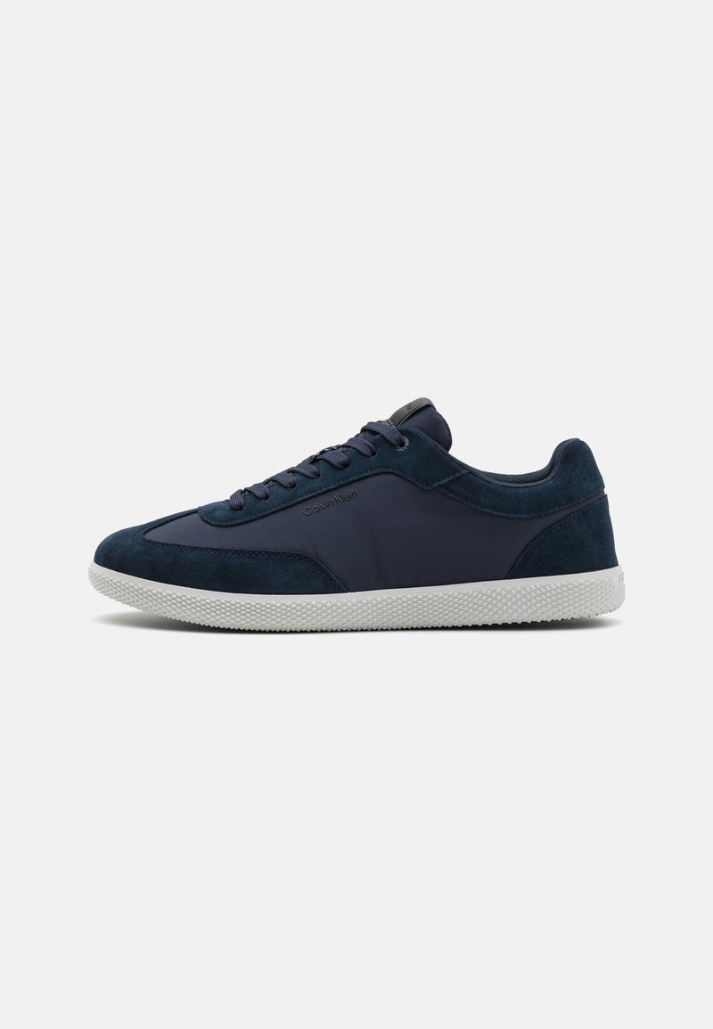 Baskets basses bleu marine avec panneaux en daim et tissu, semelle blanche texturée et fermeture à lacets.