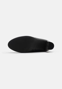 Zapato negro con parte superior de cuero suave, puntera redondeada y tacón bajo. Suela de goma texturizada con ligeras ranuras para un mejor agarre. Diseño minimalista.