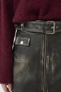 Black leather skirt with a distressed finish, featuring a front zipper, a small pocket, and a silver button. Paired with a burgundy knit sweater.