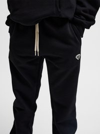 Sorte joggingbukser med beige snore og et lille hvidt bi-logo på hoften, båret med en matchende sort sweatshirt.