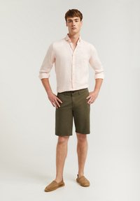 Ljusrosa linneskjorta med knäppning fram, rullade ärmar, olivgröna shorts och tan slip-on-skor. En enkel, avslappnad sommaroutfit.