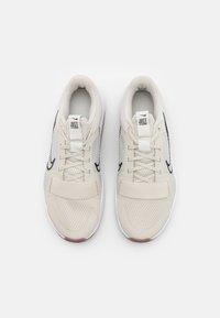 Scarpe da ginnastica beige con tomaia in rete, punta testurizzata, suola bianca e dettagli neri. Presentano un design con lacci e una fascia in tessuto.