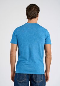 Himmelblå T-shirt med korta ärmar och rund halsringning, tillverkad av melerat tyg. Mörk denimjeans syns vid midjan.