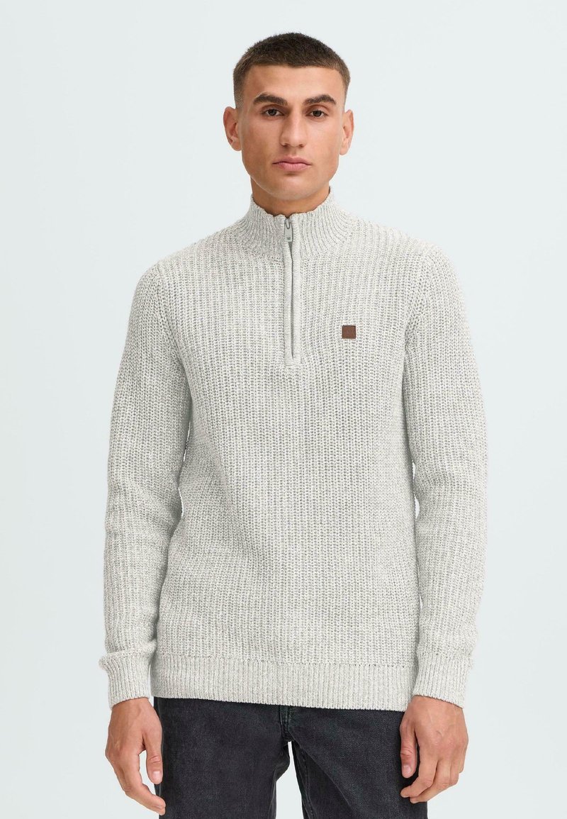 Hellgrauer, strukturierter Strickpullover mit einem Viertelreißverschluss, gerippten Bündchen, einem flachen Kragen und einem kleinen braunen Logo-Patch auf der Brust.