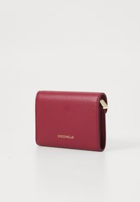 Compact burgundy leather wallet with a pebbled texture, featuring a gold logo and a metal clasp accent. Closed design.