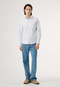 Gaiši zila svītraina garā piedurkne krekls apvienots ar gaiši ziliem džinsiem un bēšiem slaidiem apaviem. Vienkāršs, ikdienas dizains ar pogu priekšpusi.