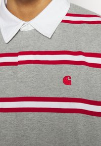 Grau Polohemd mit einem weißen Kragen. Verfügt über rot-weiße horizontale Streifen und ein kleines rotes besticktes Logo auf der Brust.