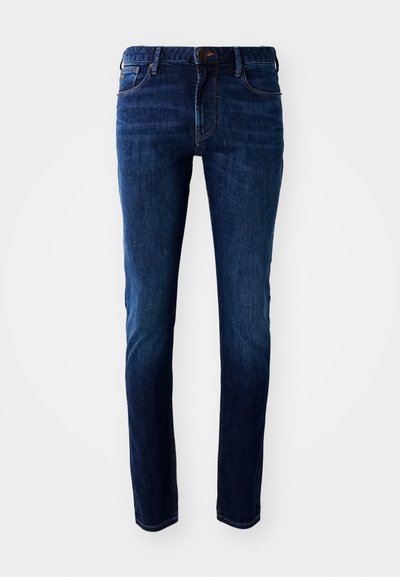 Jeans em denim azul escuro com um corte slim, apresentando um design de bolso frontal, passadores de cinto e fecho com botão. Textura suave, com áreas ligeiramente desbotadas.