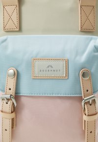 Backpack featuring a three-tone design: pale green, blue, and pink. Made of textured fabric with leather straps and metal accents. Brand label visible.