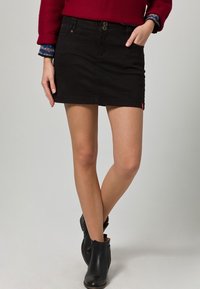 Mustat farkuhameet, joissa on kaksi etupainiketta, suora leikkaus, reiden keskiväliin saakka ulottuva pituus, jossa on pieni punainen logotagi helman lähellä.