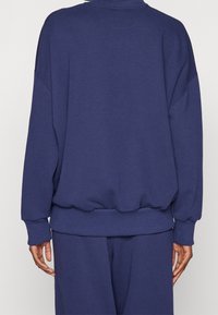 Marinblå oversized sweatshirt med rund halsringning, ribbstickade ärmslut och fåll, samt en mjuk tygtextur. Har sänkt axlar och en avslappnad passform.