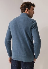 Textured blue knit sweater with a high collar, ribbed cuffs, and hem. The back features a seamless design and is softly fitted.