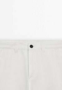 Pantaloni di cotone grigio chiaro con chiusura a bottone, passanti per cintura e tasche standard; superficie liscia senza motivi visibili.