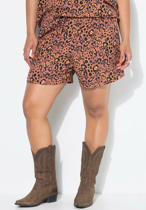 Pantaloni corti con stampa leopardata in arancione e nero, dotati di una cintura elastica, abbinati a stivali da cowboy marroni con dettagli di cucitura.