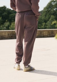 Pruunid dressipüksid lõdva lõikega, elastse vöökohaga ja ühe tagataskuga, kombineeritud heledate tossudega, millel on sinised triibud.