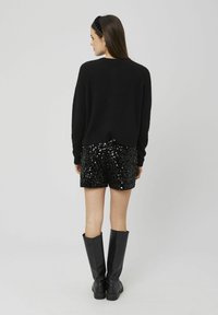 Pull noir en peluche, shorts noirs pailletés et bottes noires jusqu'aux genoux. Texture lisse, coupe décontractée et éclat des sequins.