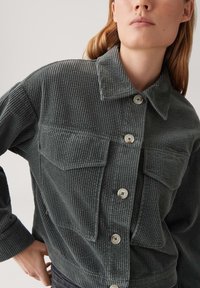 Grijze corduroy jas met een knoopsluiting aan de voorkant, twee borstzakken, een kraag en ribbeltextuur. Zilveren knopen zijn opvallende details.