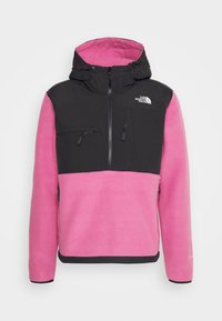 Chaqueta de forro polar con capucha en rosa y negro. Presenta un cierre frontal, dos bolsillos con cremallera y una textura suave con bloques de color en contraste.