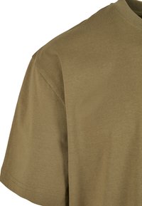 Tricou din bumbac de culoare verde măsliniu, cu mâneci scurte și gât rotund, având o textură netedă și un tiv drept.