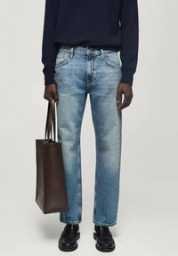 Vaqueros de denim azul claro con corte recto, combinados con un bolso de cuero marrón oscuro y zapatos negros. Los vaqueros presentan detalles de desgaste y costuras.