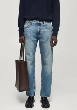 Jeans in denim azzurro chiaro con taglio dritto, abbinati a una borsa tote in pelle marrone scuro e scarpe nere. I jeans presentano dettagli di scolorimento e cuciture.