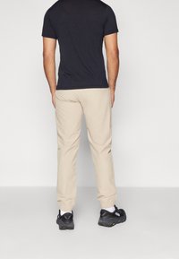 Černé tričko s krátkým rukávem v kombinaci se béžovými kalhotami s elastickými manžetami a černými teniskami. Oblečení má jednoduchý, ležérní design.