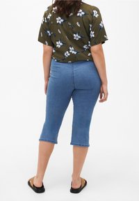 Vaqueros de mezclilla azul claro, recortados, con un diseño ajustado y dobladillo sin rematar. Combinados con una blusa de manga corta de color verde oscuro con estampado floral.