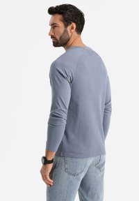 Pitkähiha, ribattua t-paitaa vaaleansinisessä, joka on varustettu pyöreällä kaula-aukolla ja tiukalla muotoilulla, yhdistettynä vaaleisiin farkkuihin.