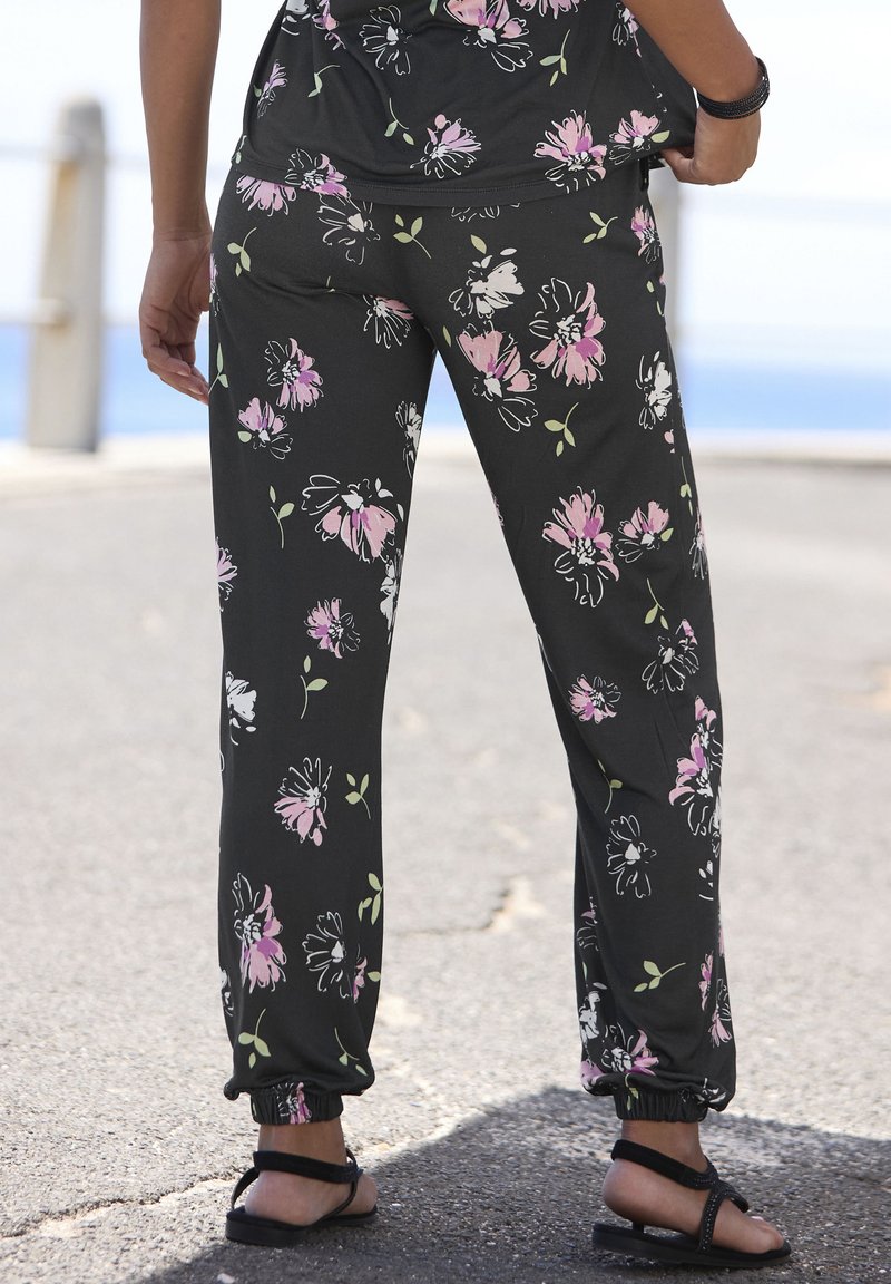 Black floral pants with pink and white flowers, elastic cuffs, and a loose fit. Material appears soft and lightweight.