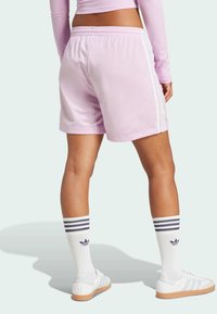 Rozā sporta bikses ar baltām sānu svītrām, ar elastīgu jostu un gludu audumu. Modelis valkā baltas kedas un svītrainas zeķes.