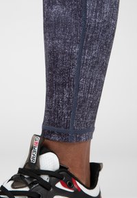 Leggings in een donkerblauw en grijs gemêleerd patroon, met een aansluitend ontwerp en contrasterende stiksels, gecombineerd met een zwart sportshoe.