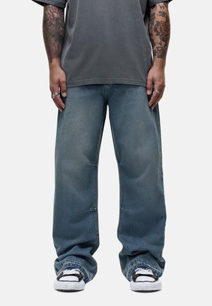 Light blue baggy jeans with a faded look, featuring a high waist and prominent stitching. Worn with a gray t-shirt and sports shoes.