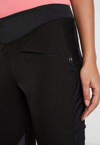 Černé sportovní kalhoty vyrobené z elastického materiálu, s postranní kapsou na zip, hladkým povrchem a kontrastní černou síťovinou.