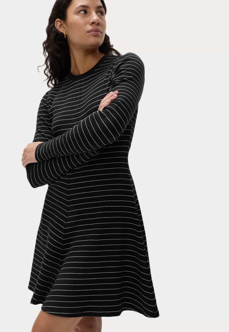 Zwart-wit gestreepte jurk met lange mouwen, een aangesloten top en een uitlopende rok. Zachte stof met een gladde textuur en een ronde halslijn.
