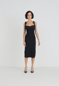 Μαύρο midi φόρεμα με εφαρμοστό μπούστο και δέσιμα λουριά. Λείο ύφασμα, απλός σχεδιασμός, μέχρι το γόνατο, σε συνδυασμό με μυτερές μαύρες γόβες.