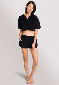 Polo shirt nera accorciata con colletto e maniche corte, abbinata a pantaloni corti neri coordinati caratterizzati da una vita elastica e tasche laterali.