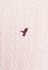 Cable-knit sweater in light pink with textured pattern; features a maroon embroidered bird accent. Soft fabric finish.