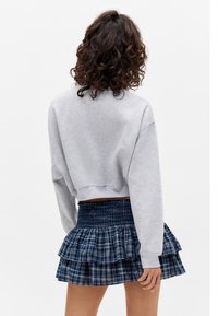Cropped gray sweatshirt with long sleeves paired with a navy plaid mini skirt featuring ruffled layers and a smocked waistband.
