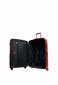 Valise rouge verticale sur roues avec poignée télescopique, ouverte pour montrer un intérieur noir avec des compartiments zippés et des sangles de rangement réglables.
