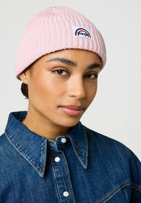 Cappellino a coste di un rosa chiaro con una piccola toppa logo multicolore. Abbinato a una camicia in denim con colletto a punta e chiusura a bottoni.