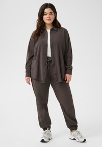 Chemise boutonnée ample gris foncé à manches longues, associée à un pantalon assorti et des baskets blanches. Texture lisse et coupe décontractée.
