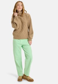 Beige gestrickter Pullover mit Rautenmuster und hohem Kragen, kombiniert mit mintgrünen Hosen und braunen Knöchelstiefeln.